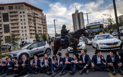 Ultra-Orthodox protesters sit on a road, blocking traffic, in front of a mounted police officer, during a demonstration against the Haredi draft, in Jerusalem, January 28, 2025. (Chaim Goldberg/Flash90)