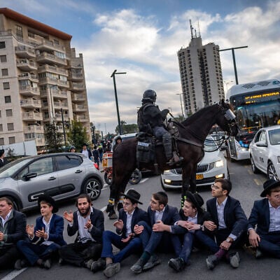 Ultra-Orthodox protesters sit on a road, blocking traffic, in front of a mounted police officer, during a demonstration against the Haredi draft, in Jerusalem, January 28, 2025. (Chaim Goldberg/Flash90)