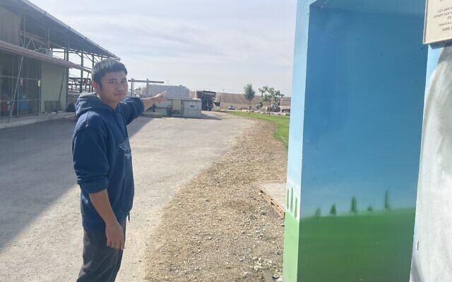 Korawit Kaeokoed, a cowshed worker at Kibbutz Alumim who is known as Kuay, pointing toward Gaza in December 2024, outside the shelter where many of his fellow Thai farm workers were killed in the Hamas terror onslaught of October 7, 2023 (Jessica Steinberg/Times of Israel)