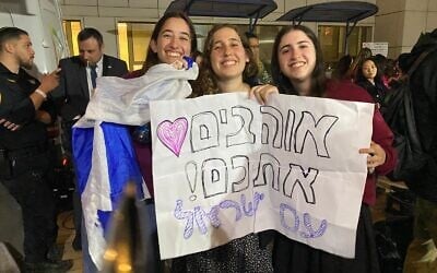 Avishag Gadot, center, with her friends, waiting at Sheba Medical Center as three hostages released from Gaza are set to arrive for treatment, January 19, 2025. The poster says: 'The people of Israel love you.' (Shoshanna Solomon/Times of Israel)