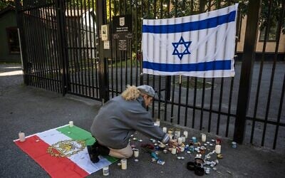 A woman lights a candle to show support outside the Israeli embassy in Stockholm, Sweden, on October 9, 2023, after the October 7 Hamas-led terror onslaught on Israel. On the fence is affixed an Israeli flag, and on the ground is the pre-Islamic Republic flag of Iran. (Jonathan Nackstrand / AFP)