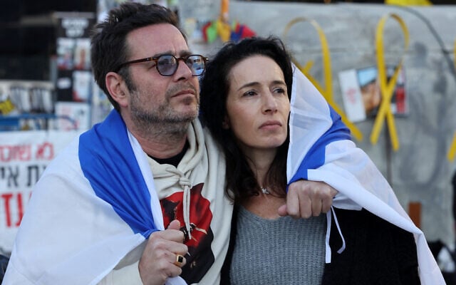 A man and a woman draped in an Israeli flag watch the release by the Hamas terror group of hostages Ofer Calderon and Yarden Bibas in the Gaza Strip, on a screen at Hostages Square in Tel Aviv,  on February 1, 2025.  (Photo by Jack GUEZ / AFP)