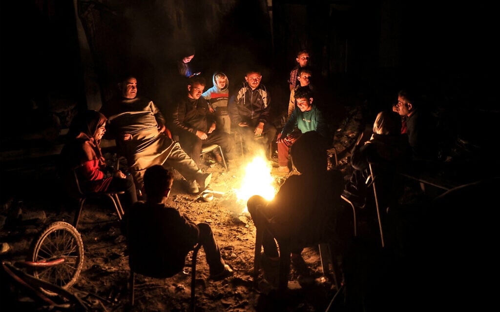 Palestinians sit by a fire outside amid the ruins of their houses in Jabalia in the northern Gaza Strip on February 18, 2025 (Omar AL-QATTAA / AFP)