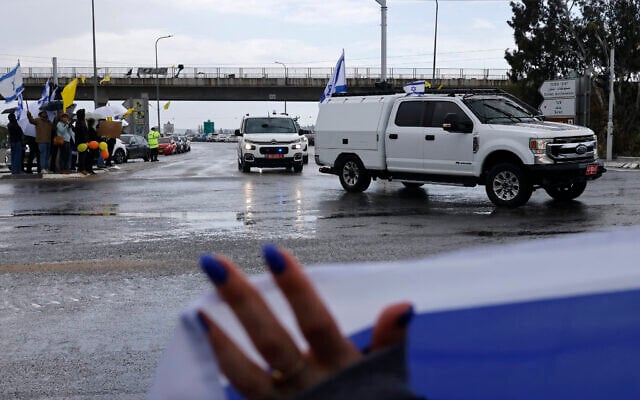 Israelis wave the national flag as a convoy transporting what is believed to be the bodies of the four Israeli hostages handed over by Hamas, passes near the southern city of Sderot on February 20, 2025. (John Wessels/AFP)