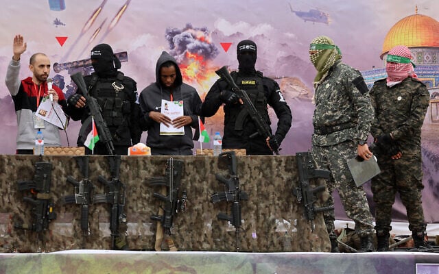 Hostages Tal Shoham (left) and Avera Mengistu (third from left), surrounded by armed fighters, stand on a stage in Rafah as they are released by the Hamas terror group in Rafah on February 22, 2025. (Omar AL-QATTAA / AFP)