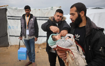 A Palestinian man holds a baby as a medic administers a polio vaccine at a camp for displaced people in Nuseirat in the central Gaza Strip on February 23, 2025. (Eyad BABA / AFP)