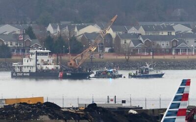 An American Airlines plane passes in the foreground as a member of a dive team and a US Coast Guard vessel with a crane work near the wreckage of a Black Hawk helicopter in the Potomac River, on January 31, 2025, in Arlington, Virginia. (AP Photo/Alex Brandon)
