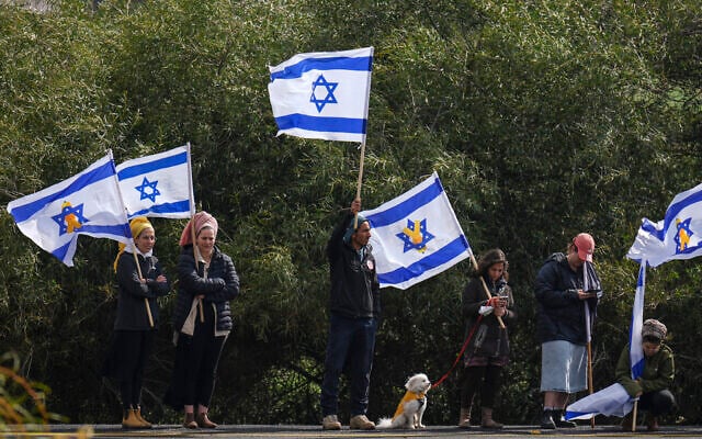 People wave Israeli flags on a road near Kibbutz Re'im, southern Israel, Feb. 20, 2025, ahead of the return by Hamas of the bodies of four Israeli hostages from the Gaza Strip. (AP Photo/Ariel Schalit)