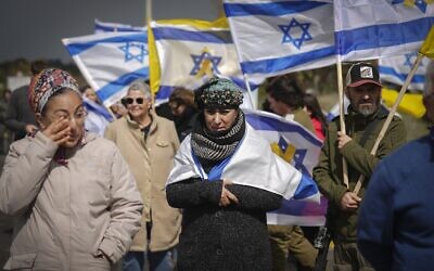 Israelis hold flags as they watch a convoy carrying coffins containing what is believed to be the bodies of four Israeli hostages that were just handed over by Palestinian terror groups in Gaza drives by near Kibbutz Re'im, southern Israel, February 20, 2025.(AP Photo/Ariel Schalit)