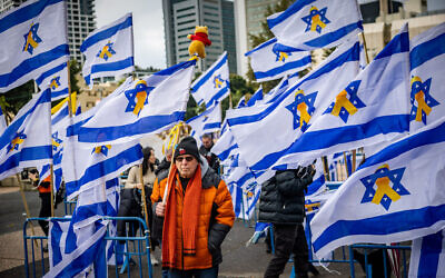 A man holds an Israeli flag featuring the yellow hostages ribbon, in Tel Aviv's Hostages Square ahead of the return of four slain Israeli hostages from Gaza, February 20, 2025. (Chaim Goldberg/Flash90)