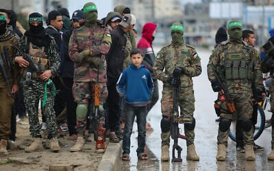 Hamas gunmen are seen with a Palestinian child at the handover event of Israeli hostages to the Red Cross, in central Gaza's Nuseirat, February 22, 2025. (Ali Hassan/Flash90)
