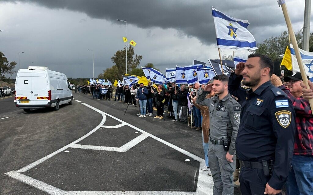 Israel Police officers salute and members of the public wave Israeli flags as a convoy carrying what are believed to be the bodies of four Israeli hostages slain in Gaza captivity makes its way to the Abu Kabir forensic institute, on February 20, 2025. (Israel Police)