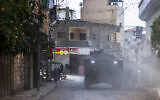 Palestinian shopkeepers look as Israeli armored vehicles drive by during a raid in the eastern neighborhood of Jenin amid a weeks-long operation in the West Bank on March 4, 2025. (Jaafar ASHTIYEH / AFP)