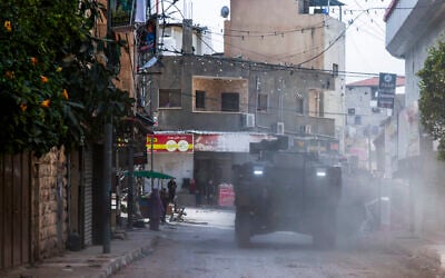 Palestinian shopkeepers look as Israeli armored vehicles drive by during a raid in the eastern neighborhood of Jenin amid a weeks-long operation in the West Bank on March 4, 2025. (Jaafar ASHTIYEH / AFP)