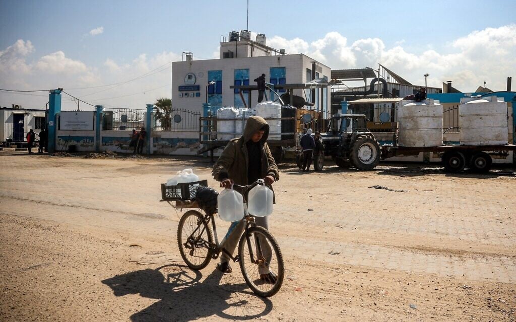 A youth pushes a bicycle loaded with filled-up water containers outside the Southern Gaza Desalination plant, which stopped working after Israel cut the electricity supply in Deir el-Balah, in the Gaza Strip, March 10, 2025. (Eyad BABA / AFP)