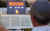 A man reads a scroll in front of a clock counting the time Israeli hostages held captive in the Gaza Strip since the October 2023 attacks by Hamas terrorists have spent in captivity, during the reading of the Megillat Esther (Book of Esther) at the start of the festival of Purim at Hostages Square in Tel Aviv on March 13, 2025. (Jack GUEZ / AFP)