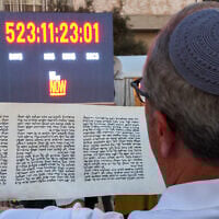 A man reads a scroll in front of a clock counting the time Israeli hostages held captive in the Gaza Strip since the October 2023 attacks by Hamas terrorists have spent in captivity, during the reading of the Megillat Esther (Book of Esther) at the start of the festival of Purim at Hostages Square in Tel Aviv on March 13, 2025. (Jack GUEZ / AFP)