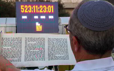 A man reads a scroll in front of a clock counting the time Israeli hostages held captive in the Gaza Strip since the October 2023 attacks by Hamas terrorists have spent in captivity, during the reading of the Megillat Esther (Book of Esther) at the start of the festival of Purim at Hostages Square in Tel Aviv on March 13, 2025. (Jack GUEZ / AFP)