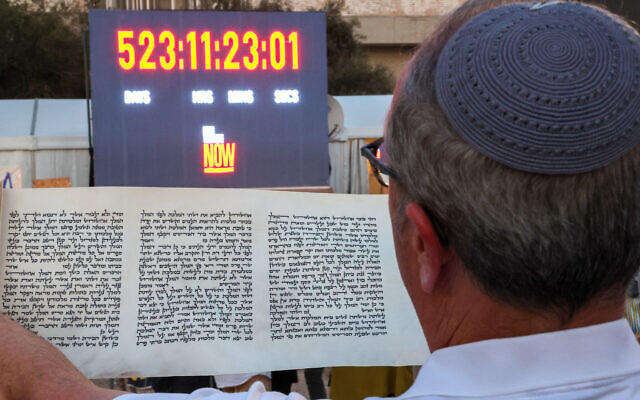 A man reads a scroll in front of a clock counting the time Israeli hostages held captive in the Gaza Strip since the October 2023 attacks by Hamas terrorists have spent in captivity, during the reading of the Megillat Esther (Book of Esther) at the start of the festival of Purim at Hostages Square in Tel Aviv on March 13, 2025. (Jack GUEZ / AFP)
