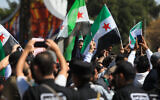 Syrian security forces stand guard as people chant and wave national flags amid celebrations on the fourteenth anniversary of the Syrian uprising, at a rally in Umayyad Square in Damascus on March 15, 2025. (Bakr AlKasem/AFP)