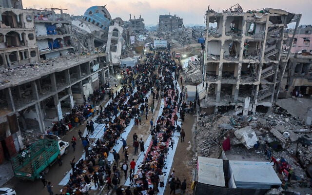 Palestinians gather for a mass fast-breaking iftar meal amid the rubble of destroyed buildings, and the ruins of the Salim Abu Muslim mosque (top-L) in Beit Lahia in the northern Gaza Strip on March 15, 2025, during the Muslim holy fasting month of Ramadan. (Omar AL-QATTAA / AFP) Palestinians gather for a mass fast-breaking iftar meal amid the rubble of destroyed buildings, and the ruins of the Salim Abu Muslim mosque (top-L) in Beit Lahia in the northern Gaza Strip on March 15, 2025, during the Muslim holy fasting month of Ramadan. (Omar AL-QATTAA / AFP)