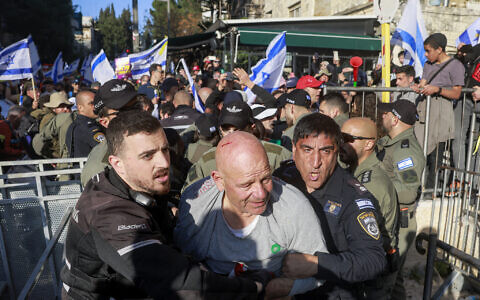 An anti-government demonstrator is seen with a cut on his head being escorted by security forces during scuffles outside the Prime Minister's Residence in Jerusalem on March 23, 2025. (Menahem Kahana / AFP)