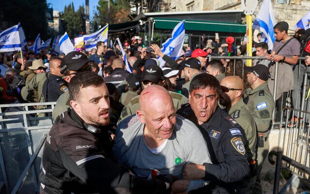 An anti-government demonstrator is seen with a cut on his head being escorted by security forces during scuffles outside the Prime Minister's Residence in Jerusalem on March 23, 2025. (Menahem Kahana / AFP)