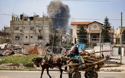 Men riding a horse-drawn cart carrying chopped tree branches for lumber watch as a smoke plume erupts from a building that was hit by an Israeli strike after prior warning in Nuseirat in the central Gaza Strip on March 25, 2025 (Eyad BABA / AFP)
