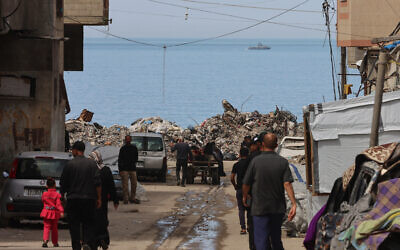 An Israeli Navy boat sails off Gaza City in the Mediterranean Sea as civilians walk in a seashore alley, on March 28, 2025 (Omar AL-QATTAA / AFP)