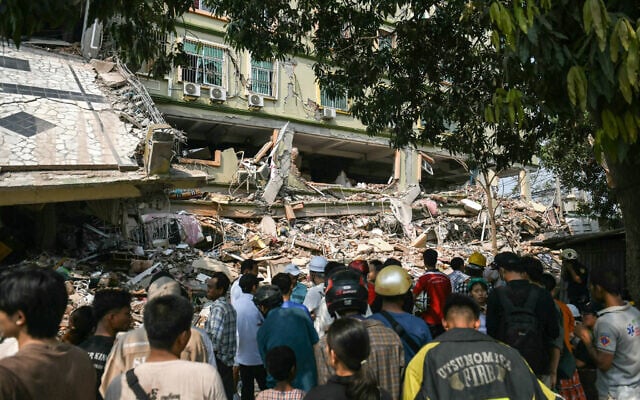 People look on as teams of rescue workers attempt to free residents trapped under the rubble of the destroyed Sky Villa Condominium development in Mandalay on March 29, 2025, a day after an earthquake struck central Myanmar. (Sai Aung MAIN / AFP)