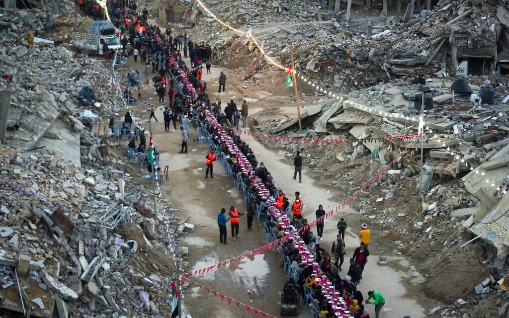 Palestinians sit at a large table surrounded by the rubble of destroyed homes and buildings as they gather for iftar, the fast-breaking meal, on the first day of Ramadan in Rafah, southern Gaza Strip, Saturday, March 1, 2025 (AP Photo/Abdel Kareem Hana)
