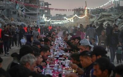 Palestinians sit at a large table surrounded by the rubble of destroyed homes and buildings as they gather for iftar, the fast-breaking meal, on the first day of Ramadan in Rafah, southern Gaza Strip, March 1, 2025 (AP Photo/Abdel Kareem Hana)