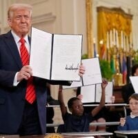 US President Donald Trump holds up a signed executive order as young people hold up copies of the executive order at an education event in the East Room of the White House in Washington, March 20, 2025. (AP/Ben Curtis)