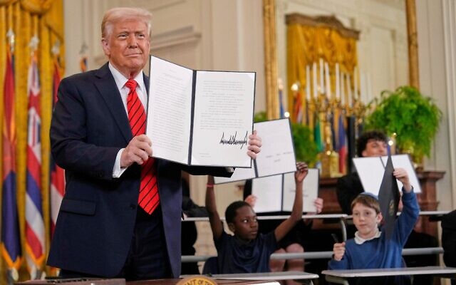 US President Donald Trump holds up a signed executive order as young people hold up copies of the executive order at an education event in the East Room of the White House in Washington, March 20, 2025. (AP/Ben Curtis) US President Donald Trump holds up a signed executive order as young people hold up copies of the executive order at an education event in the East Room of the White House in Washington, March 20, 2025. (AP/Ben Curtis)