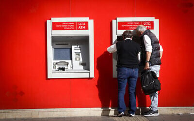A woman takes out money from a Bank HaPoalim ATM machiine in Tel Aviv on December 9, 2024. (Miriam Alster/FLASH90)