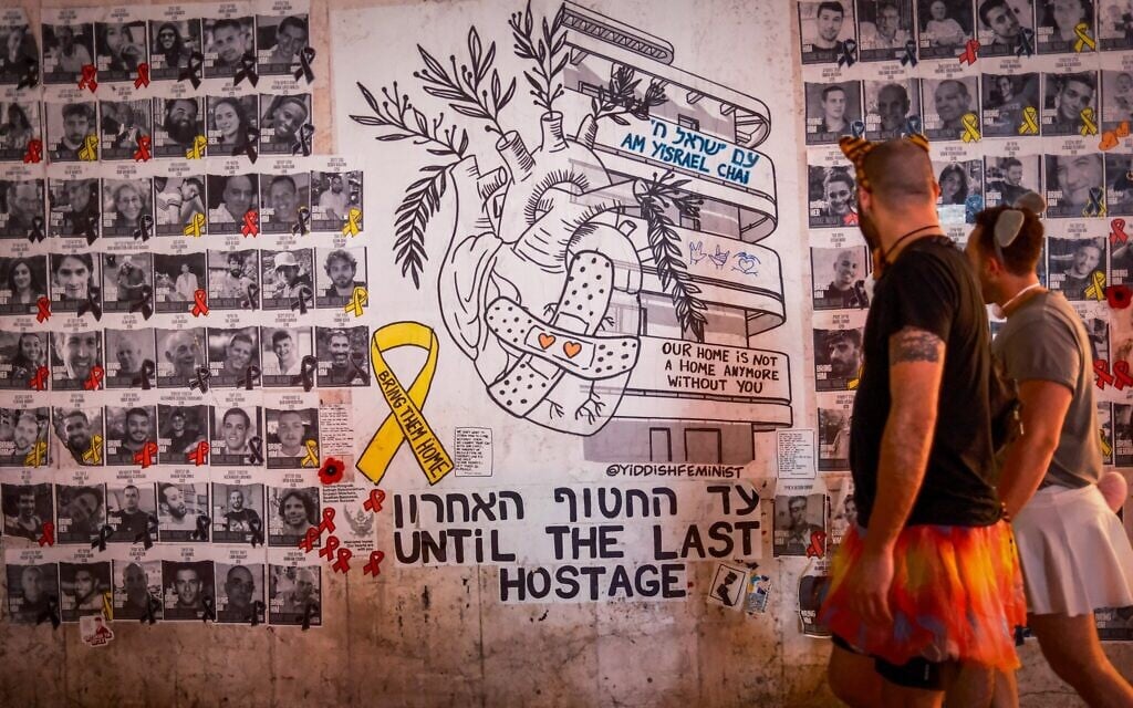 People wearing costumes walk by posters of hostages held in Gaza, on the Jewish festival of Purim in Tel Aviv, March 13, 2025. (Dor Pazuelo/Flash90)