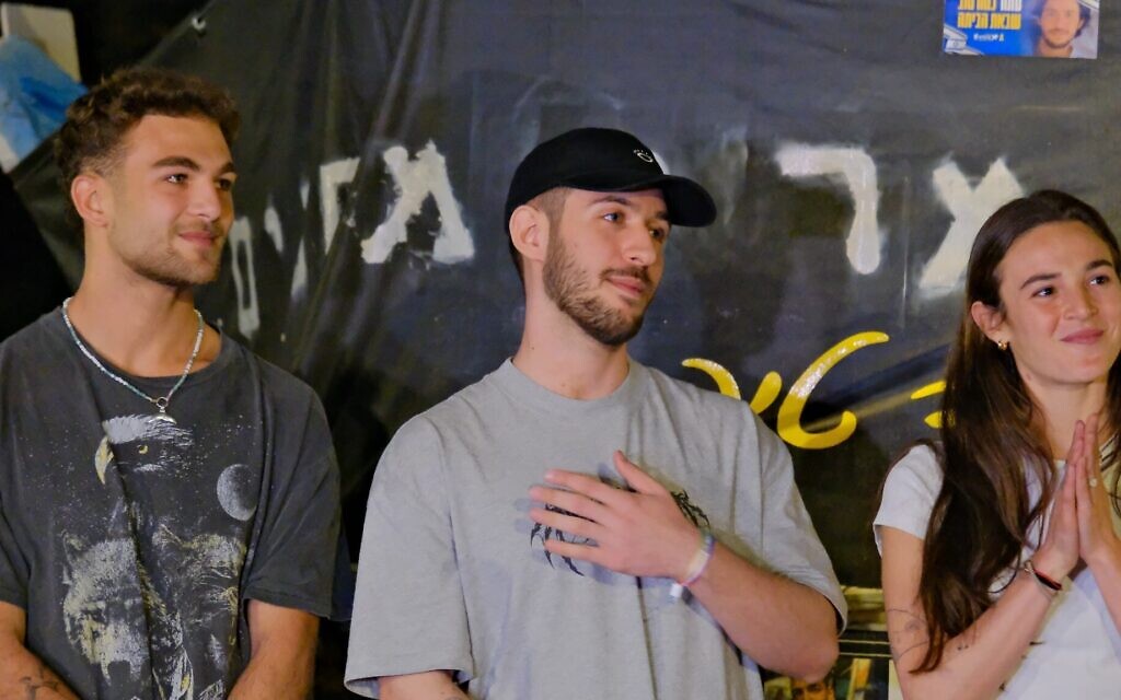 Released hostage Omer Shem Tov (center) stands with Itay (L) and Maya Regev as he addresses a crowd gathered to watch him take down a banner calling for his release, Herzliya, March 13, 2025. (Adar Eyal/Pro-Democracy Protest Movement)