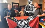 Members of the racist British Movement unfurl a flag with a swastika and SS imagery at the Duke of Edinburgh pub (who say they weren't aware) in Royton, England on April 20, 2025, in celebration of Adolf Hitler's birthday. An image of Hitler has been superimposed onto the image. (British Movement)