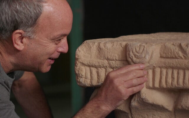 Israel Antiquities Authority archaeologist Dr. Uzi Ad with the ancient capital decorated with menorahs discovered in Jerusalem, which will be displayed for the first time in May 2025. (Emil Aladjem/Israel Antiquities Authority)