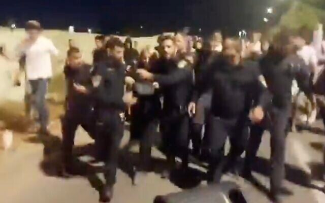 Police escort a woman away from right-wing rioters who disrupted a screening at Ra'anana's Beit Samueli synagogue of the joint Israeli-Palestinian Memorial Day ceremony, April 29, 2025. (X screenshot)
