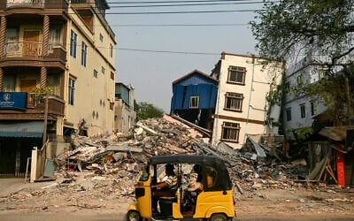 A three-wheeled motorcycle drives past collapsed and damaged buildings in Mandalay, after the March 28 earthquake struck central Myanmar, April 3, 2025. (AFP/ Sai Aung MAIN)