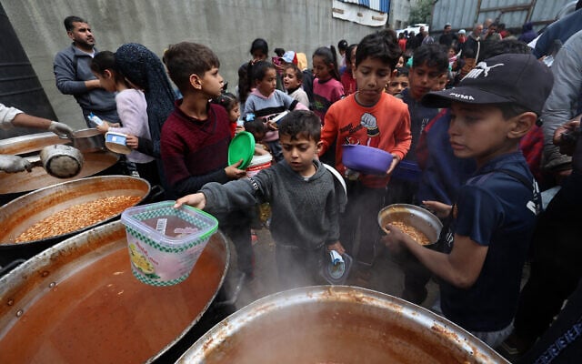 Palestinian children receive their portion of a hot meal at a free food distribution point  in the Nuseirat refugee camp in the central Gaza Strip on April 12, 2025. (Eyad BABA / AFP)
