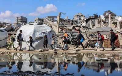 People walk past a puddle of water by a tent shelter erected near the rubble of a collapsed building in the Nasr neighborhood in western Gaza City on April 15, 2025. (Omar AL-QATTAA / AFP)