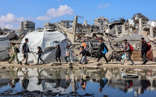 People walk past a puddle of water by a tent shelter erected near the rubble of a collapsed building in the Nasr neighborhood in western Gaza City on April 15, 2025. (Omar AL-QATTAA / AFP)