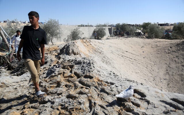 A Palestinian youth walks around a large crater caused by an Israeli strike at a camp for displaced Palestinians in northern Khan Younis in the southern Gaza Strip on April 19, 2025. (AFP)