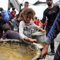 A girl stands with a pot as people queue to receive charity meals from a kitchen in Beit Lahia in the northern Gaza Strip on April 24, 2025 (Bashar TALEB / AFP)