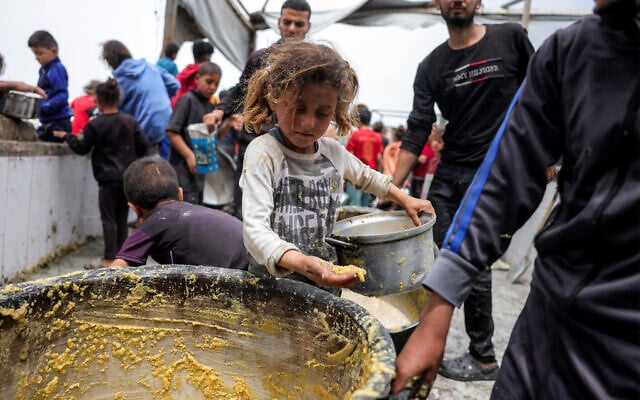 A girl stands with a pot as people queue to receive charity meals from a kitchen in Beit Lahia in the northern Gaza Strip on April 24, 2025 (Bashar TALEB / AFP)