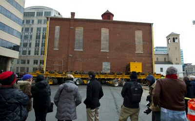 Illustrative: People watch workers move the Adas Israel Synagogue, the oldest synagogue in Washington, to a new location down the street, where it became part of the Capital Jewish Museum, on January 9, 2019, in Washington, DC. (AP Photo/Jose Luis Magana)