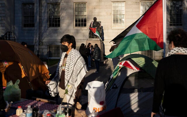 A student protester stands in front of the statue of John Harvard, the first major benefactor of Harvard College, draped in the Palestinian flag, at an encampment of students protesting against the war in Gaza, at Harvard University in Cambridge, Mass., April 25, 2024. (AP Photo/Ben Curtis, File)