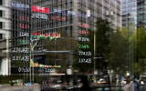 Pedestrians and office buildings are reflected on the window of a brokerage house as an electronic board displays trading data in the Central Business District, in Beijing, China, April 9, 2025. (AP Photo/Andy Wong)